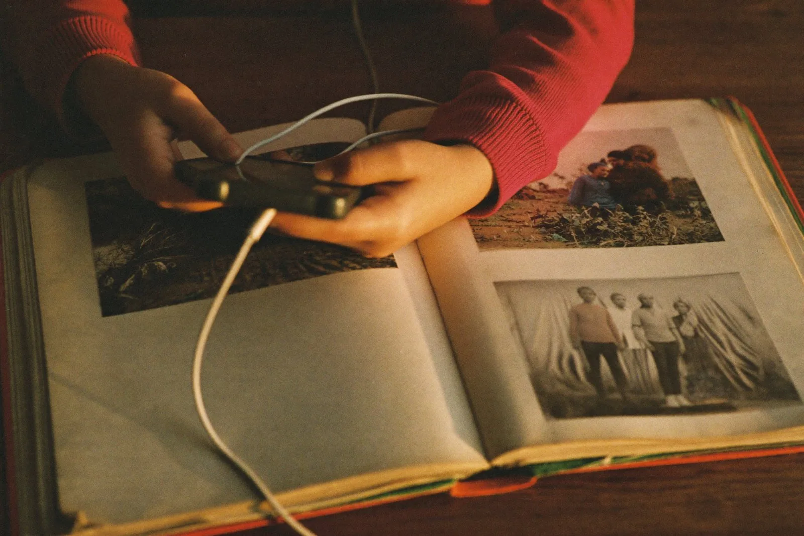 A child's hands holding a phone and headphones over an open family photo album